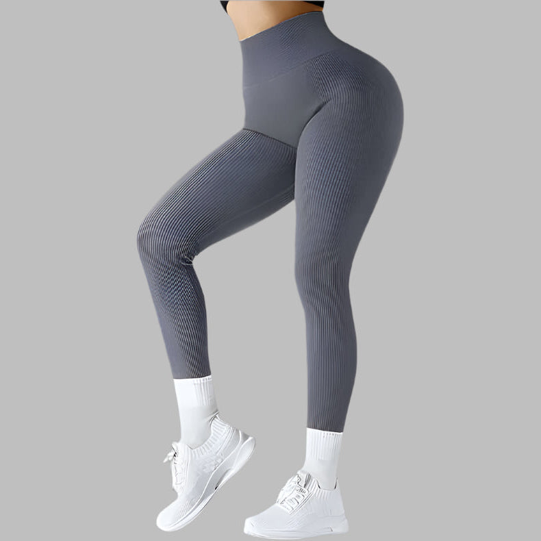 Gray seamless fitness leggings with ribbed texture, high-waist design shown from the side, paired with white sneakers on a gray background.