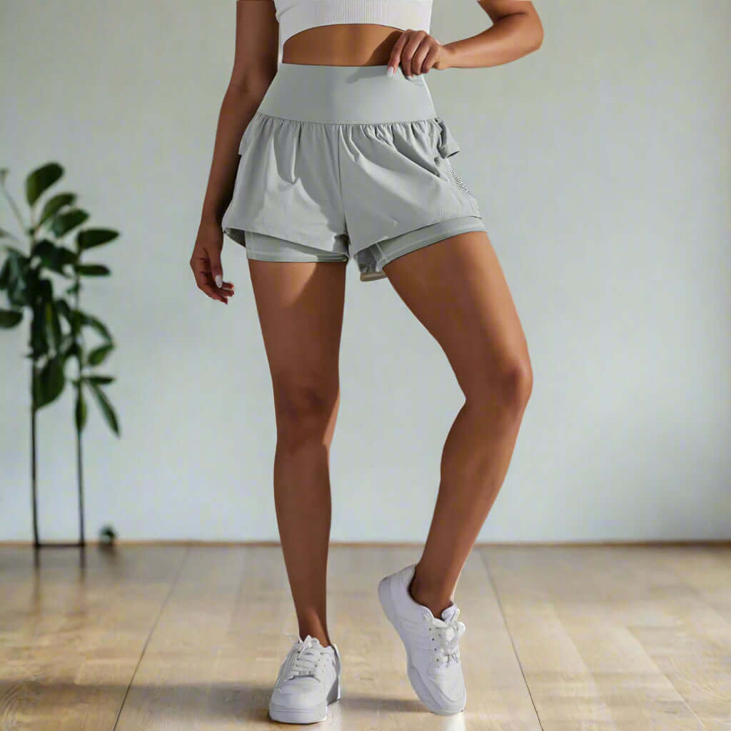 Woman wearing light gray double-layer yoga shorts with high-waist design, ideal for workouts and active days, standing indoors.
