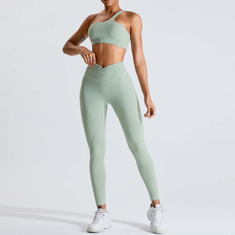 Woman wearing a mint green fashion yoga set, featuring a one-shoulder top and high-waisted leggings, standing on a plain background.