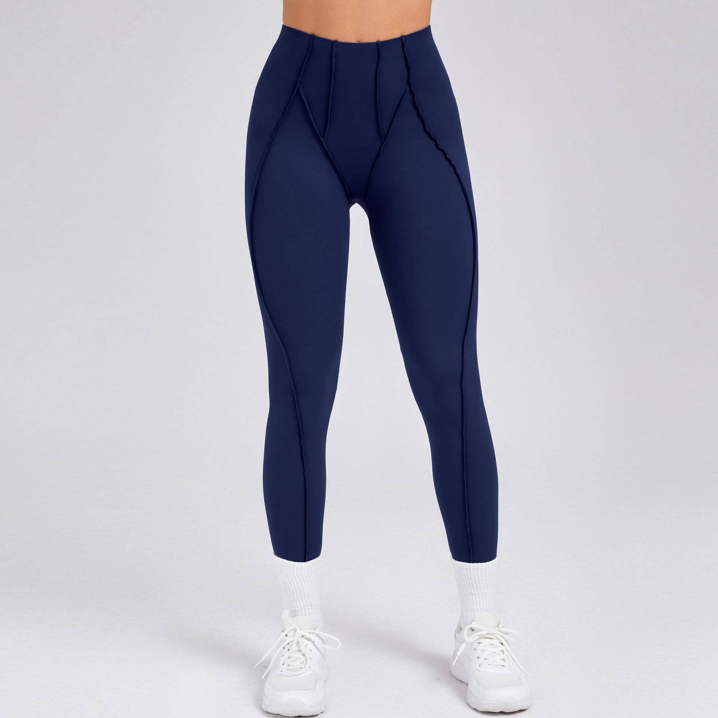 Woman wearing navy blue compression gym leggings with supportive stitching, paired with white sneakers and socks on a neutral background.