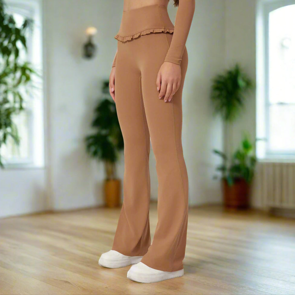 Woman wearing high waist brown leggings with a flared design and ruffle detail, paired with a matching long-sleeve top and white shoes.