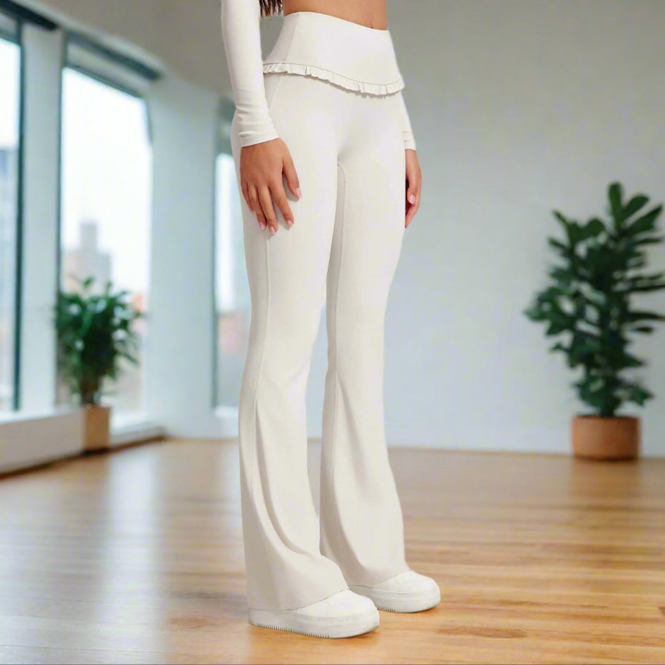 Woman wearing high waist white leggings with ruffled waistband, paired with a long sleeve crop top and white slip-on shoes.