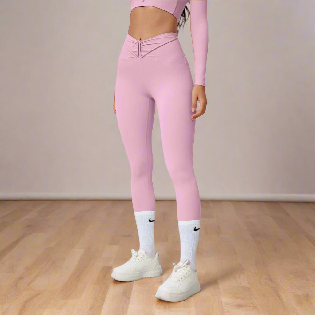 Woman wearing pink seamless shaping leggings and white sneakers on gray background