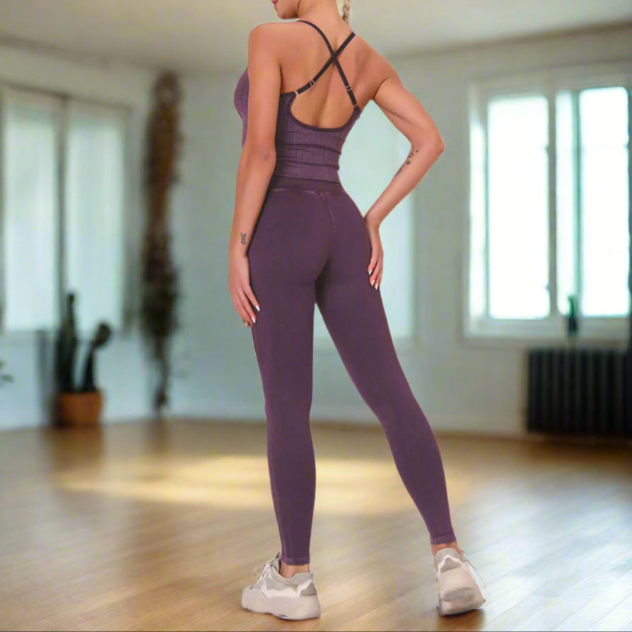 Back view of woman wearing a purple seamless suit with cross-back straps, standing against a light wall.
