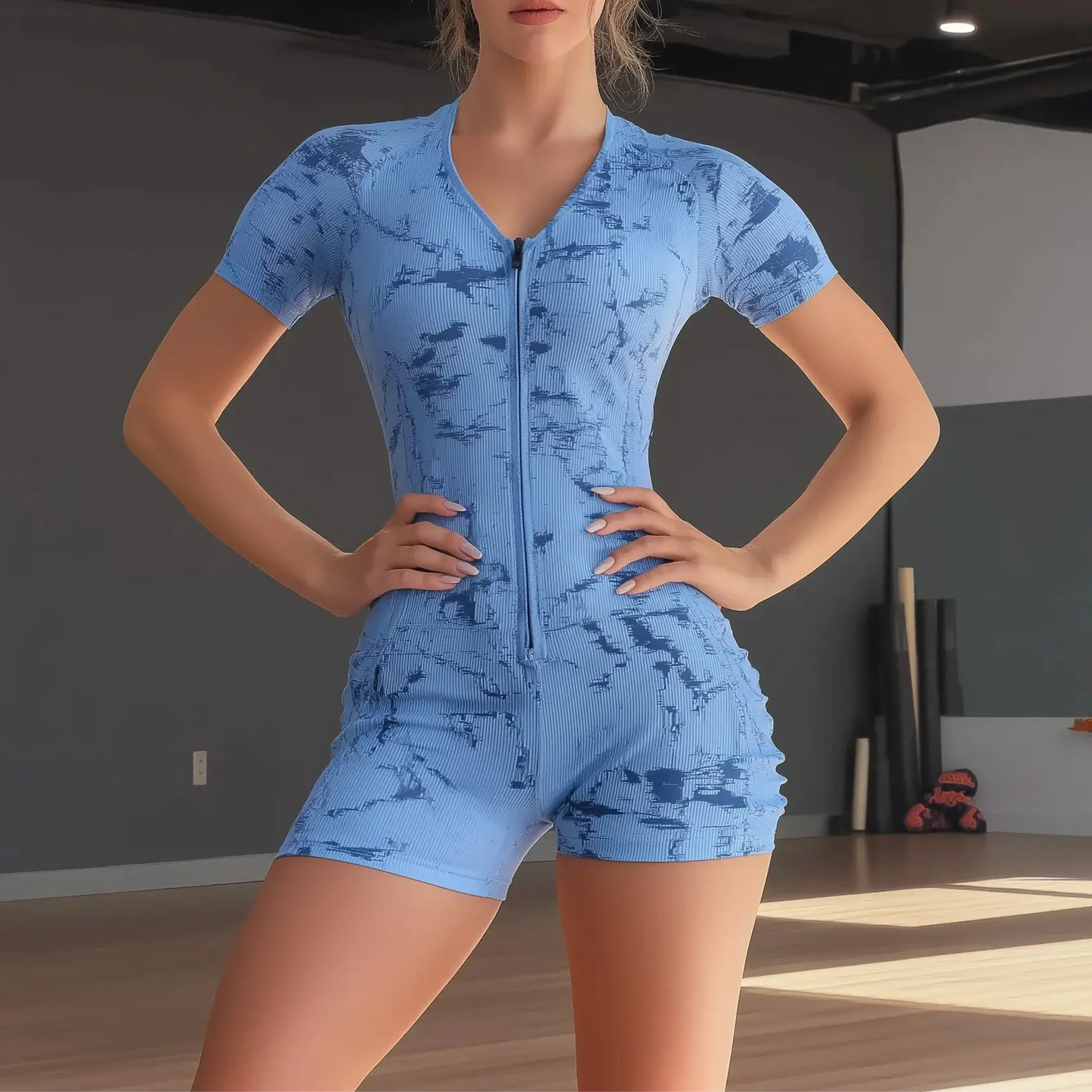 Woman wearing a blue tie-dye elastic bodysuit with short sleeves and zip closure, perfect for yoga or casual wear, in a studio setting.