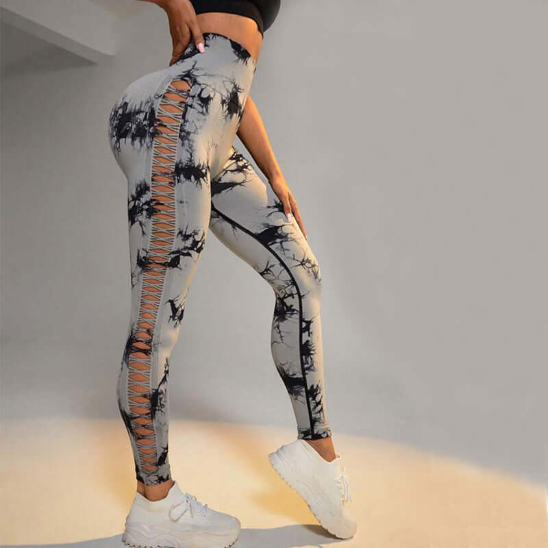 Woman wearing butt-lift gym leggings with side lace-up detailing and a tie-dye pattern, paired with white sneakers.