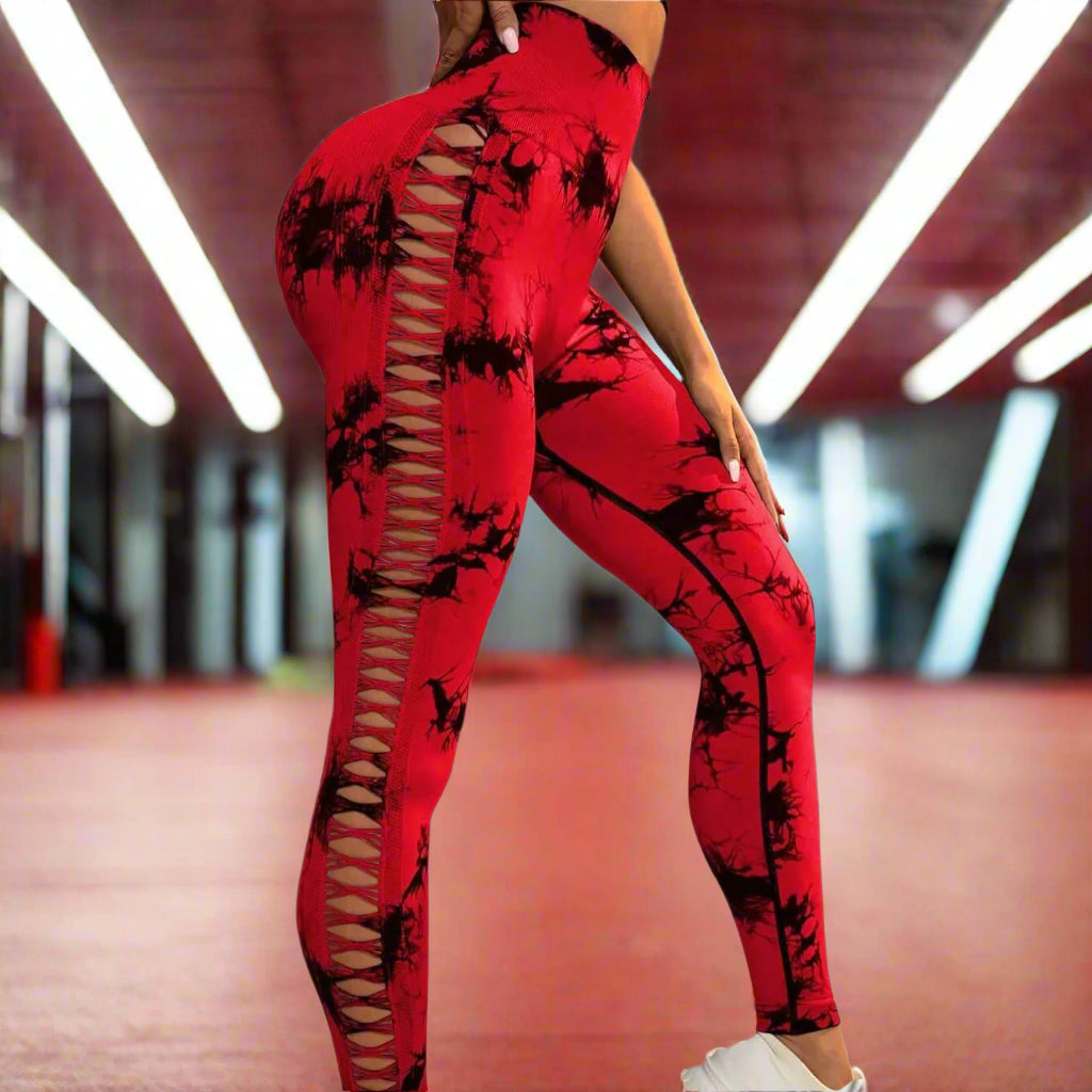 Woman wearing high-waisted red butt-lift gym leggings with lattice cut design, paired with white sneakers, showcasing stylish workout fashion.