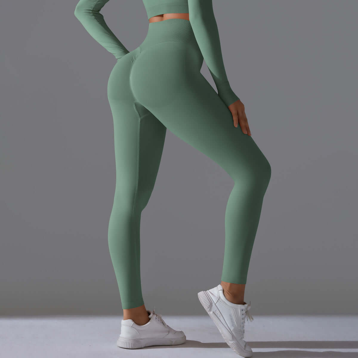 Alt Tag: Seamless high waist leggings in smoky moss green color, featuring a flattering fit, shown on model with white sneakers against gray background.