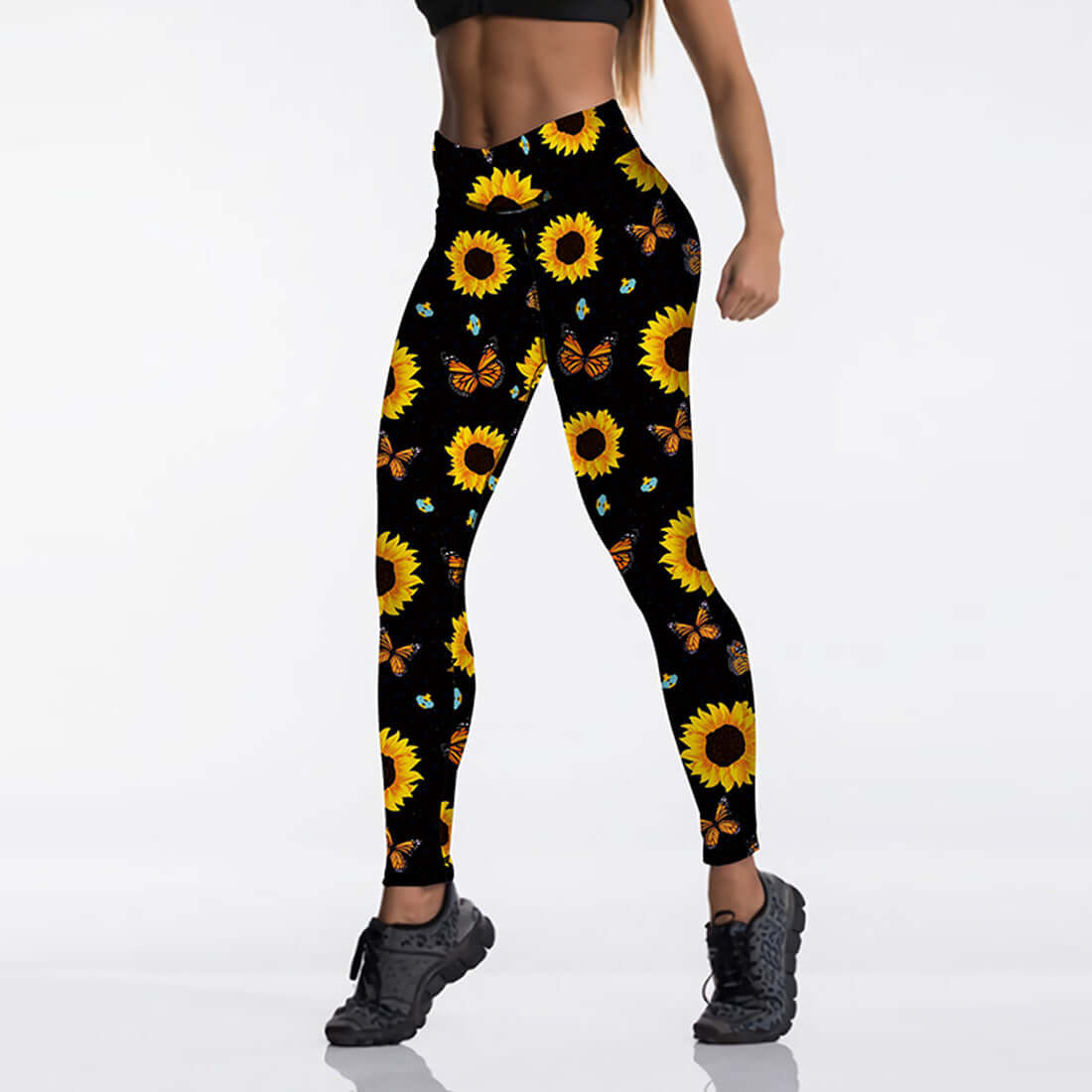 Woman modeling black leggings with bright sunflower and butterfly print, showcasing vibrant floral workout apparel.