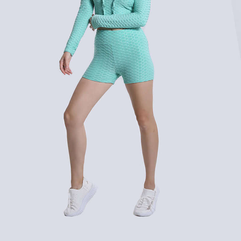 Woman wearing high waist teal textured shorts and matching top with white sneakers against a light background