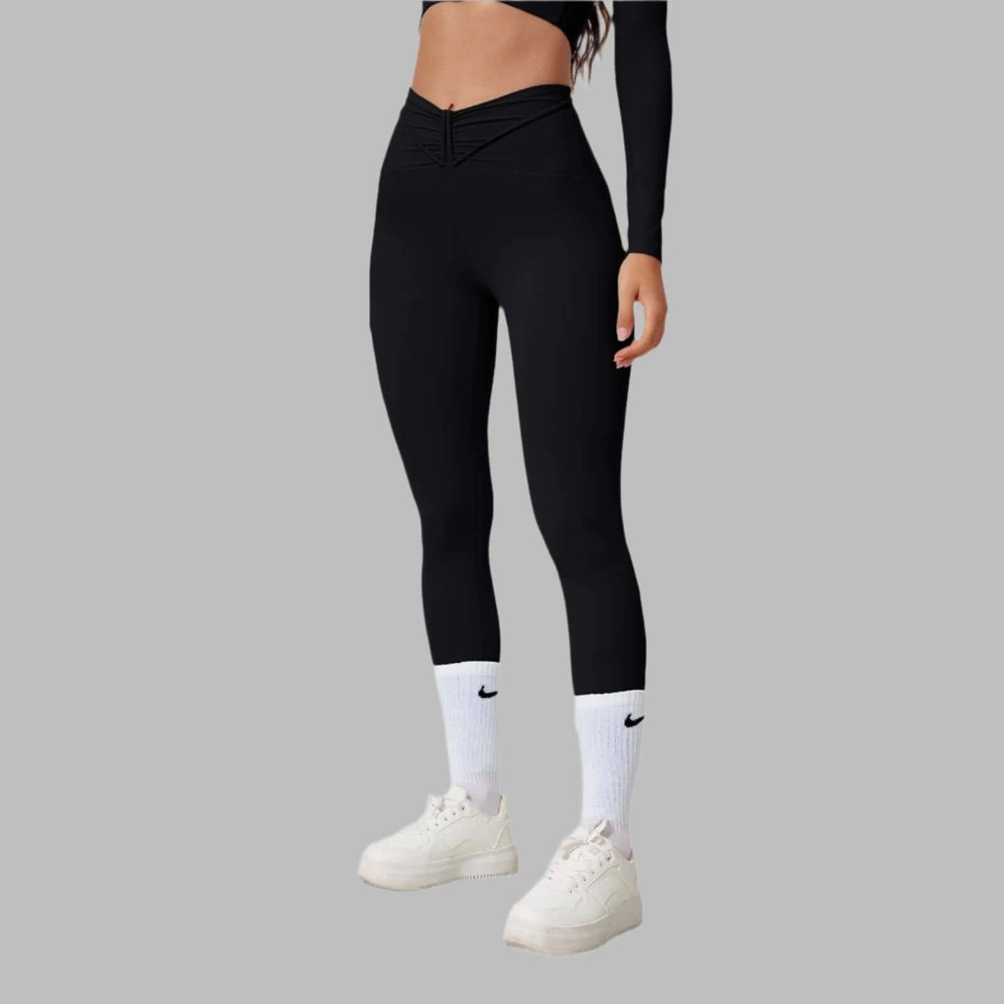 Woman wearing black seamless shaping leggings with white sneakers and socks, showcasing a comfortable and flattering fit on a gray background.