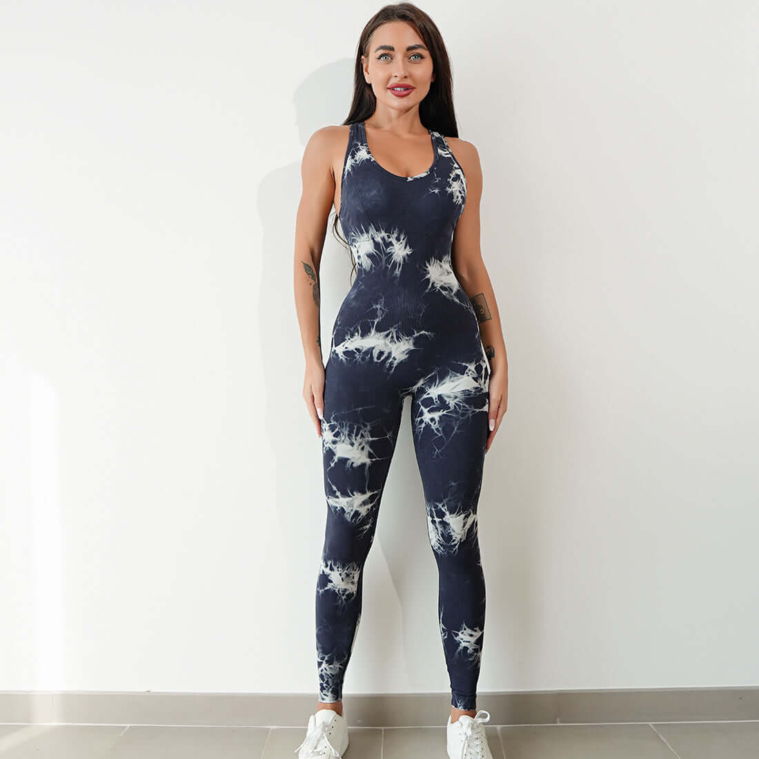 Woman modeling navy tie-dye workout jumpsuit with white sneakers, perfect for fitness and activewear fashion.