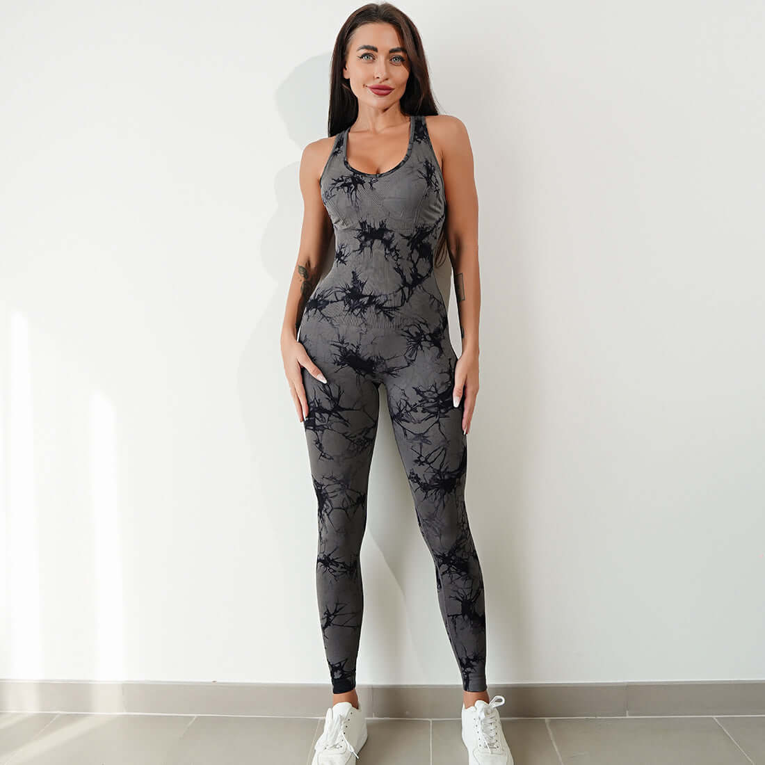 Woman wearing a stylish gray workout jumpsuit with black pattern, standing indoors on tile floor.