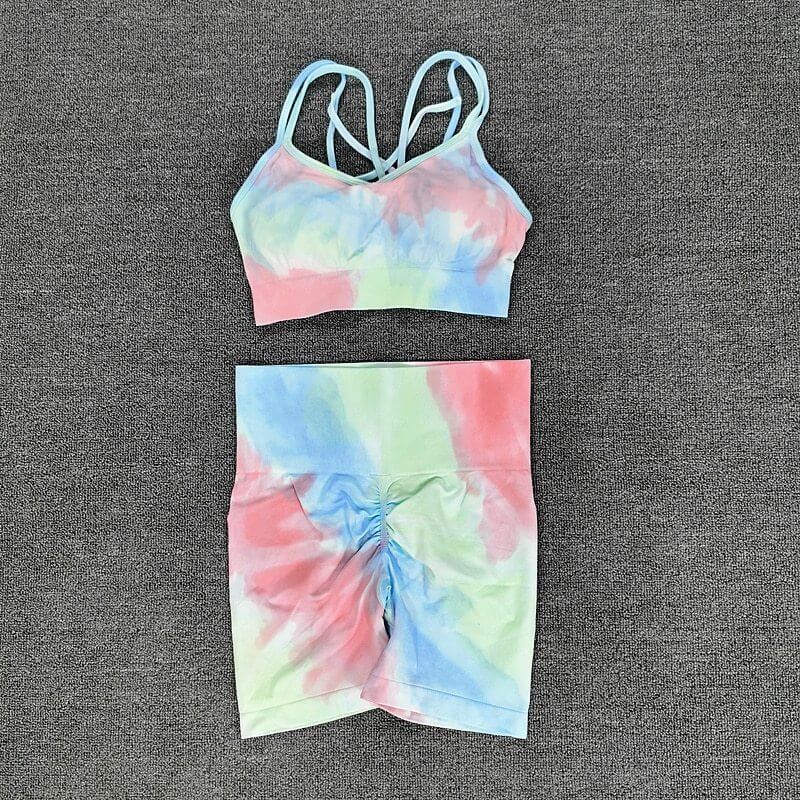 Colorful seamless sport set with tie-dye design, featuring a strappy sports bra and ruched high-waisted shorts on a gray background.