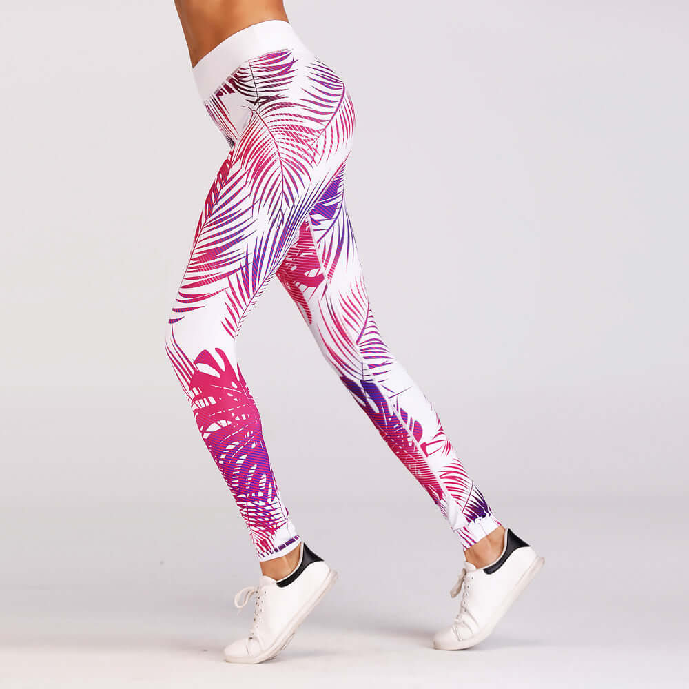 Woman wearing red print yoga leggings with a palm leaf design, showcasing flexibility in a side view against a plain background.