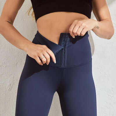 Woman wearing navy seamless compression leggings, adjusting the waistband for comfort and support in a fitness setting.