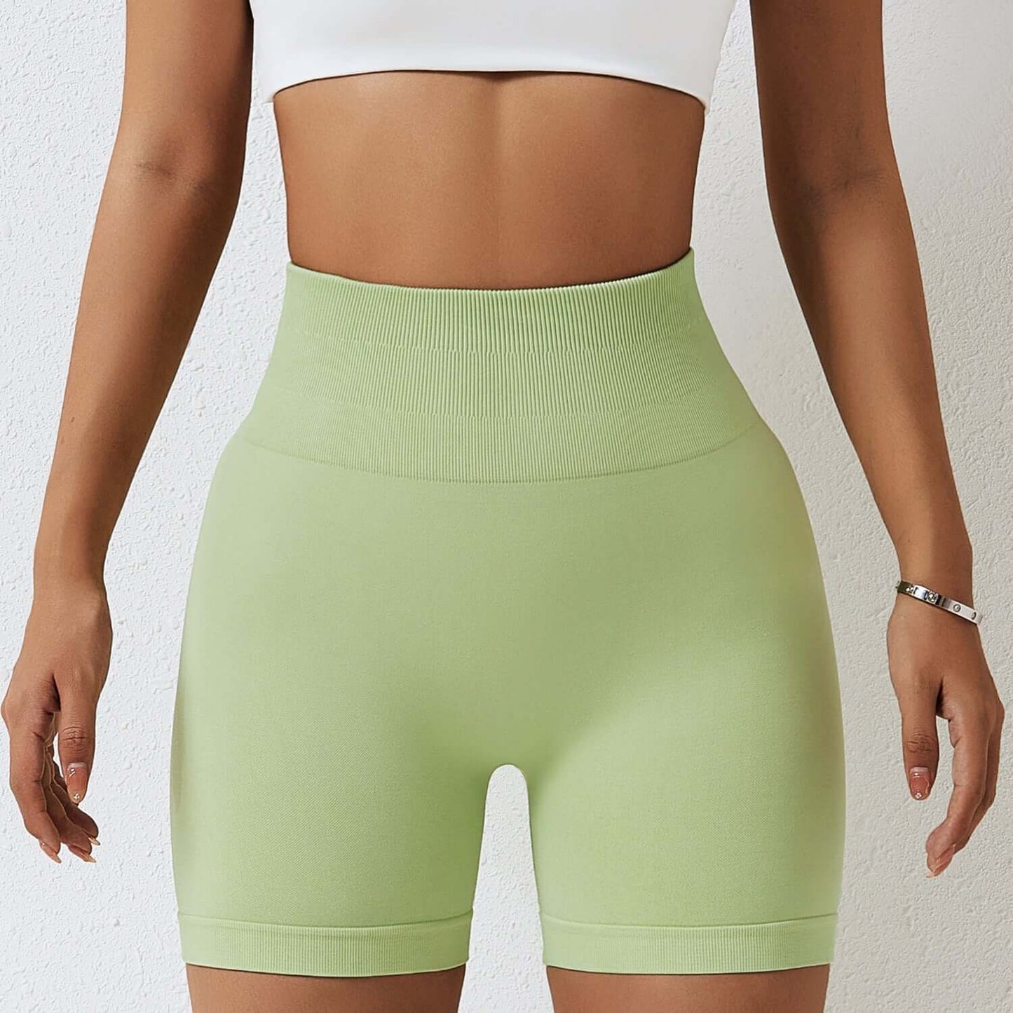 Woman wearing seamless high-waist shorts in light green, showcasing high hip support and smooth fabric design.