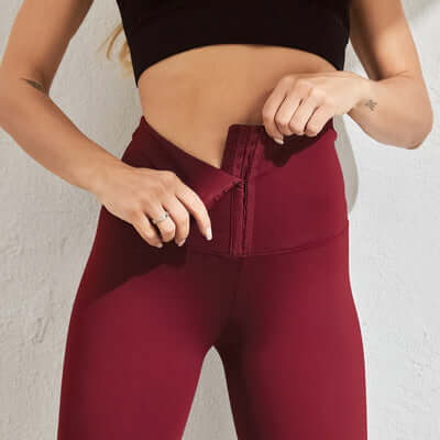 Woman wearing seamless compression leggings in burgundy, adjusting waist closure for a perfect fit.