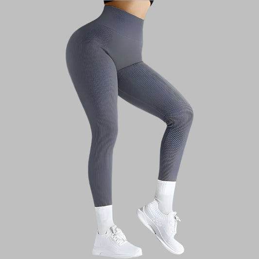 Gray seamless fitness leggings with ribbed texture, high-waist design shown from the side, paired with white sneakers on a gray background.