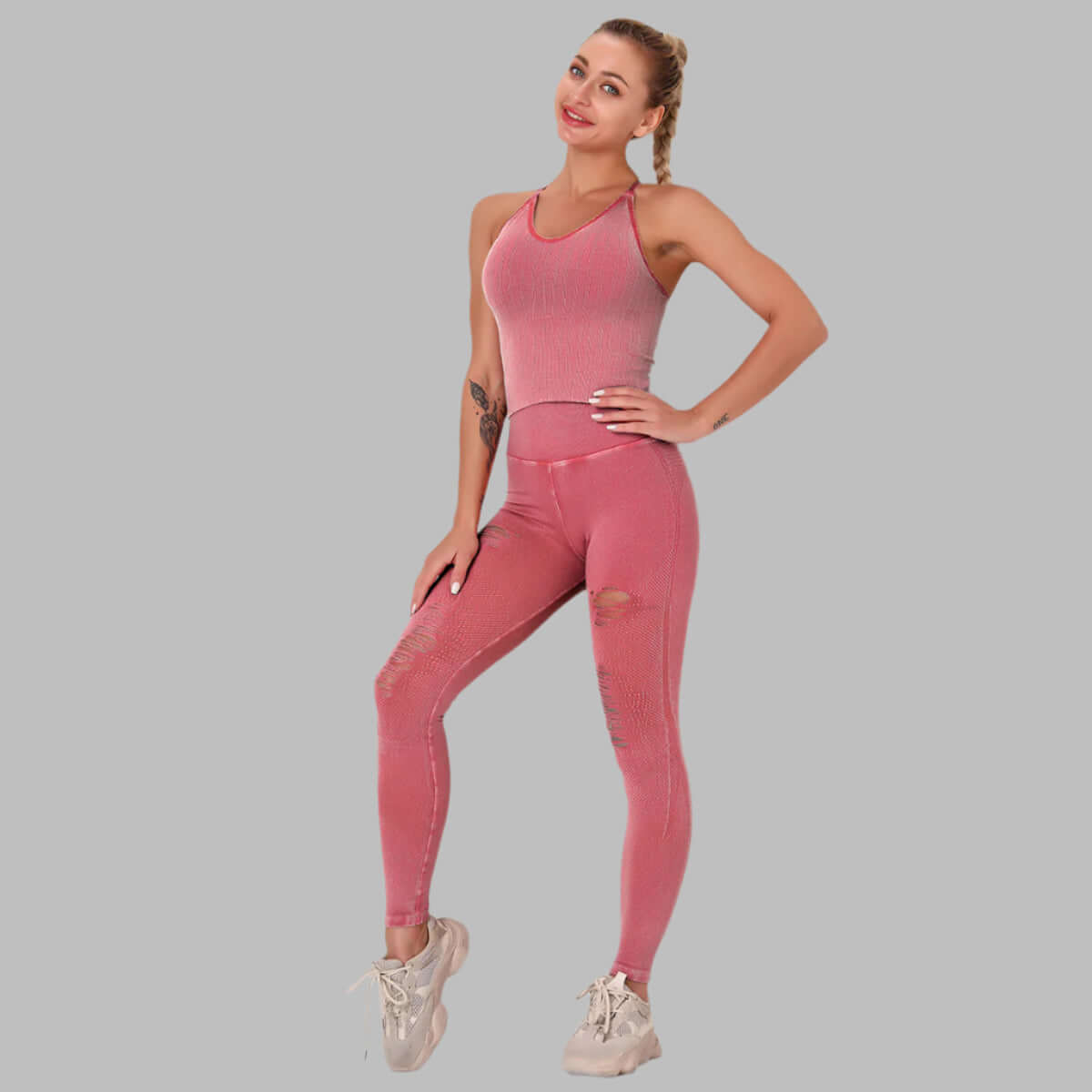 Woman wearing a pink seamless fitness suit with ripped design, standing confidently against a gray background.