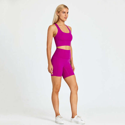 Woman wearing vibrant pink workout outfit with racerback top and shorts, standing with hands on hips.