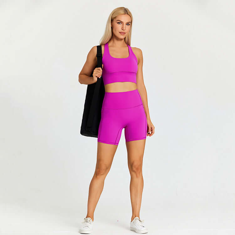 Woman in vibrant pink workout outfit holding black gym bag, showcasing stylish outdoor sport set.