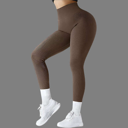 Woman wearing brown seamless fitness leggings and white sneakers against a grey background, showcasing high-waisted design and ribbed textures.