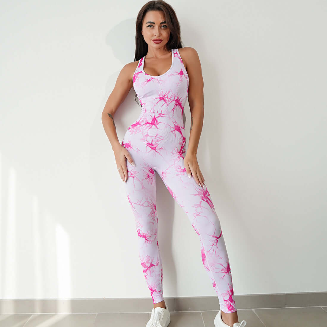 Woman wearing a pink and white compression workout bodysuit standing in a well-lit room, showcasing activewear fashion.