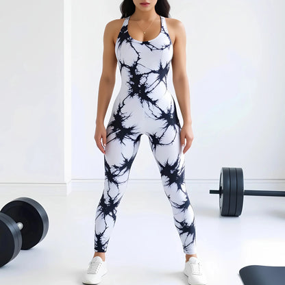 Woman wearing a black and white tie-dye compression workout bodysuit standing in a gym setting with weights on the floor.