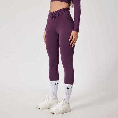 Woman wearing seamless shaping leggings in deep purple, paired with white sneakers and socks. Comfortable and stylish activewear.