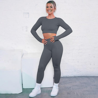 Woman wearing a seamless knitted striped suit, posing against a white brick wall, showcasing activewear style and comfort.