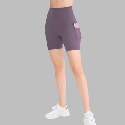 Woman wearing purple high-waisted pocket sport shorts with phone in pocket, paired with white sneakers on gray background.