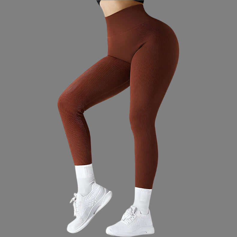 Woman wearing brown seamless fitness leggings with ribbed texture, paired with white sneakers, showcasing flexibility and style on a gray background.