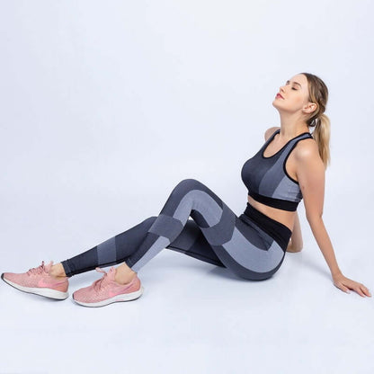 Woman wearing a black and gray seamless yoga set, sitting relaxed with pink sneakers, showcasing sporty and breathable fabric.