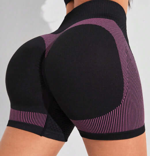 Woman wearing high waist workout shorts with pink and black design, showcasing comfortable fit and flexible fabric ideal for exercise.
