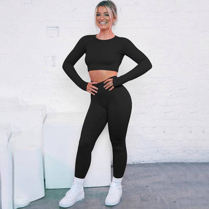 Woman wearing a black seamless knitted suit with long sleeves and stripes, posing against a white brick background.