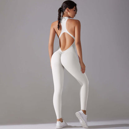 Woman wearing a white seamless workout jumpsuit with open back design and sneakers, standing against a gray background.