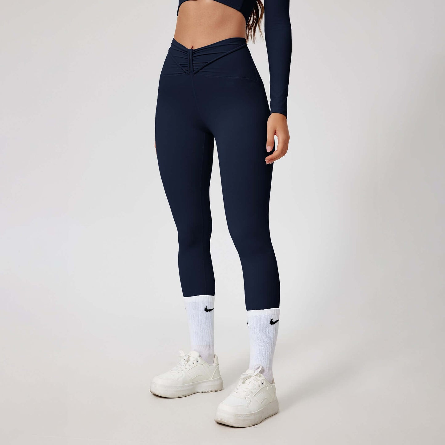 Woman wearing seamless shaping leggings in navy, showcasing sleek design and high-waisted fit, paired with white sneakers.