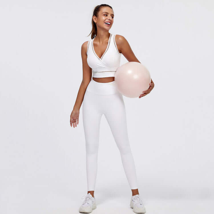 Woman wearing white hip-lifting peach trousers fitness suit with exercise ball, showcasing activewear for yoga or gym.